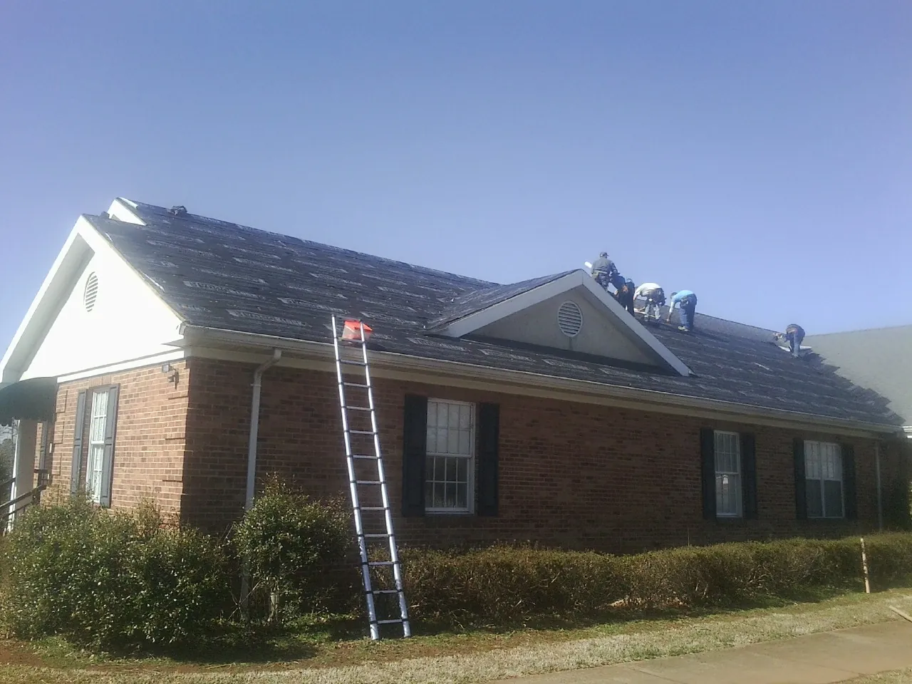 Crew tearing shingles off a brick ranch roof with a ladder set — Emergency Roof Repair work by our crew in New Bremen