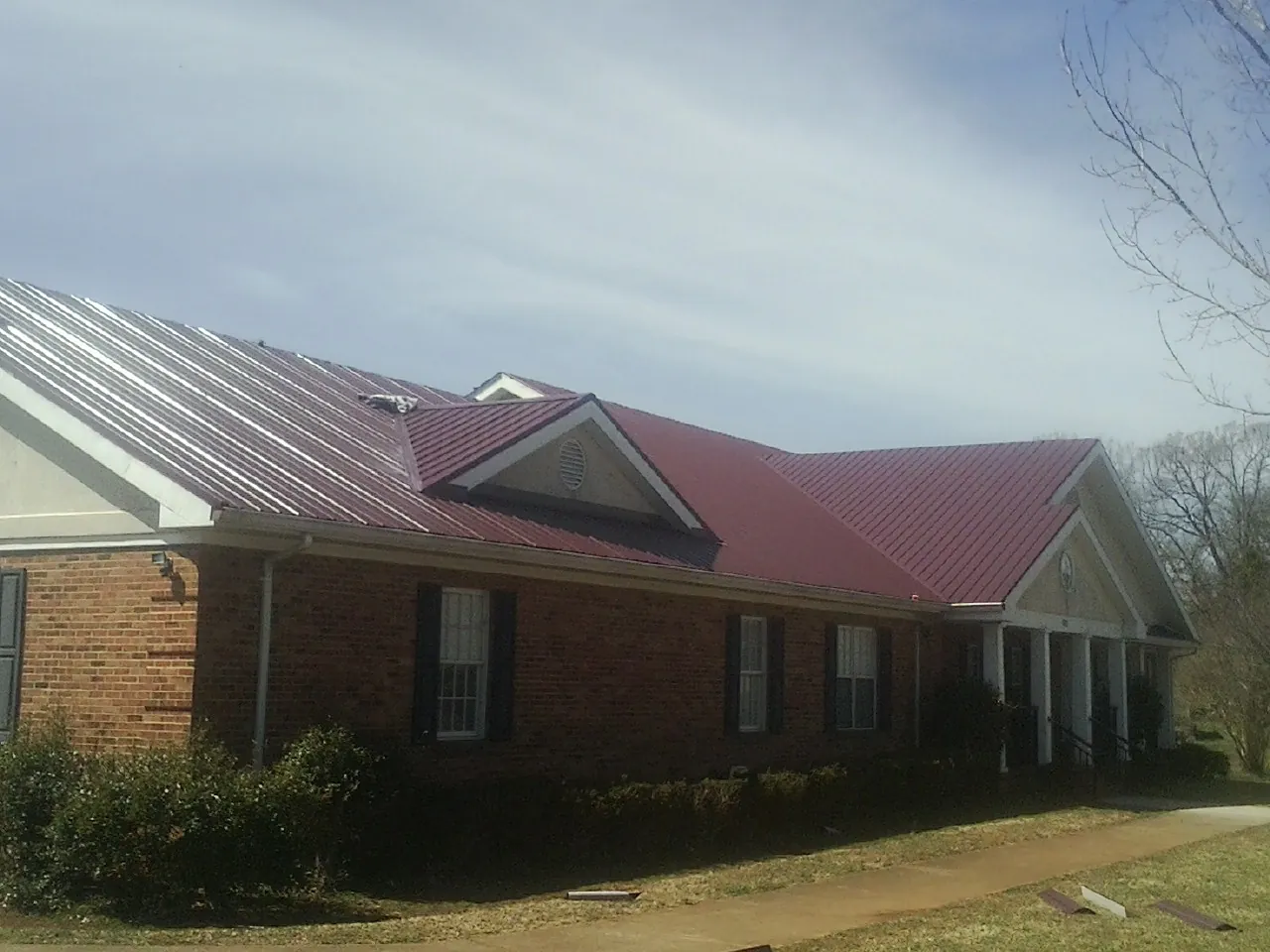 Red metal roof with gabled entries on a long brick building, from a Hail Damage Roof Repair job in New Bremen