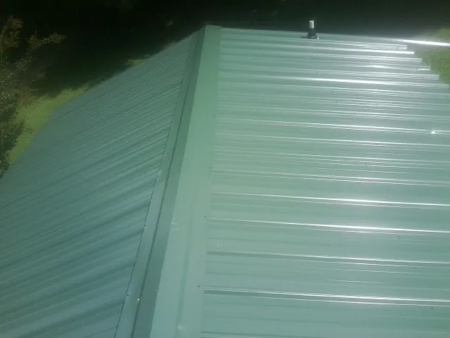 New green metal panels meeting at the ridge of a roof — Flat Roof Repair work by our crew in New Bremen