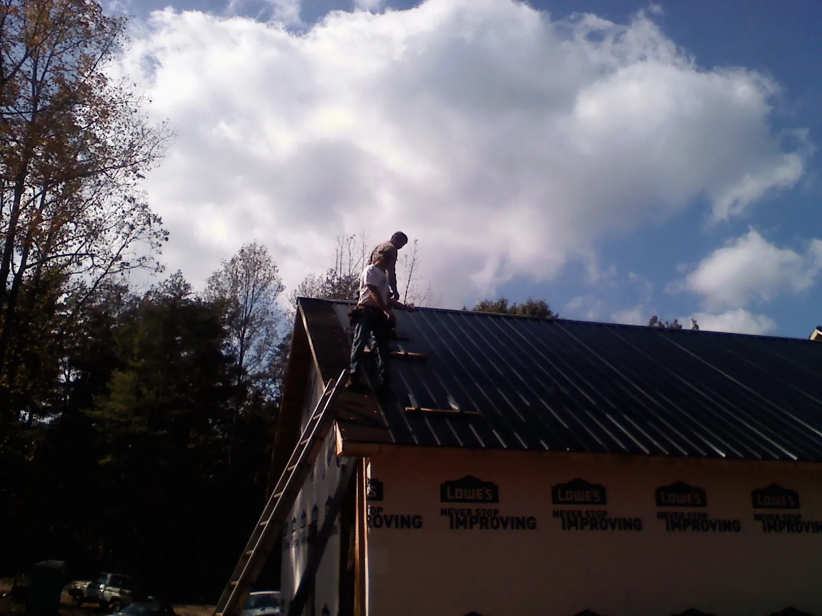 Roofer fastening dark metal panels high against a cloudy sky, from a Roof Inspection job in New Bremen
