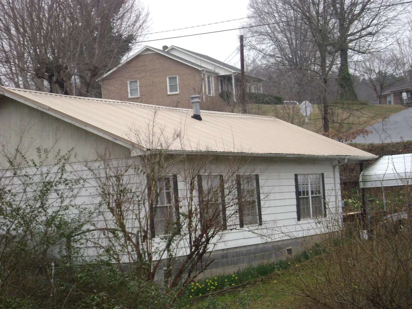 Tan metal roof on a white sided house set into a hillside — Commercial Roofing by Roofing Brothers in New Bremen